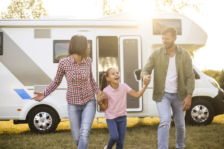 smiling family of three in front of Class C motorhome at RV park